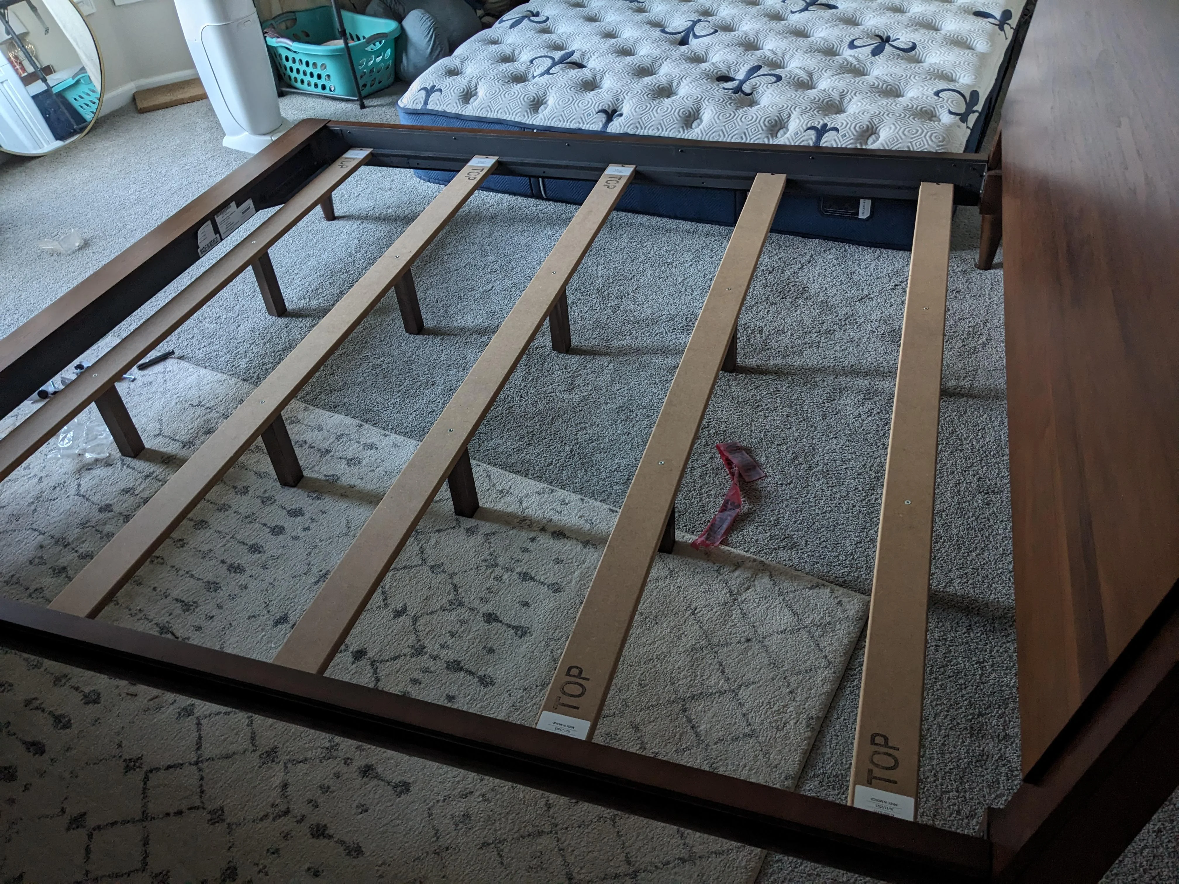 A bed frame center rail with two support legs resting flat on a hardwood floor under the slats