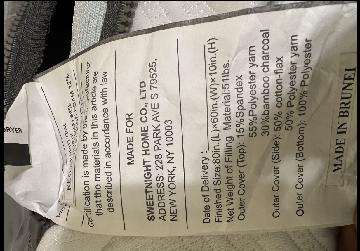 A closeup photo of a mattress law label tag sewn into the side seam, with small printed text visible