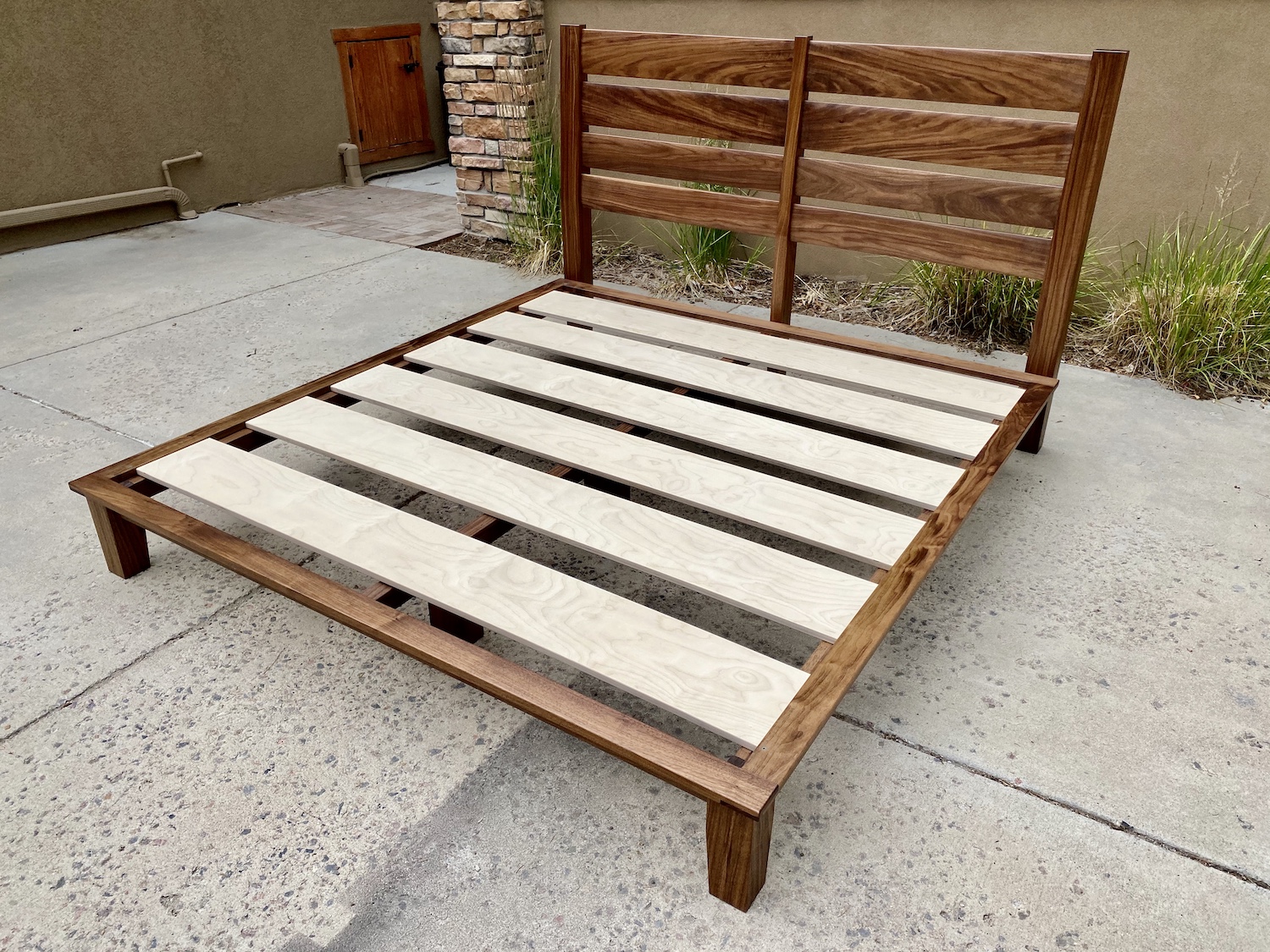 A platform bed frame with the mattress removed, showing evenly spaced wooden slats running across the frame